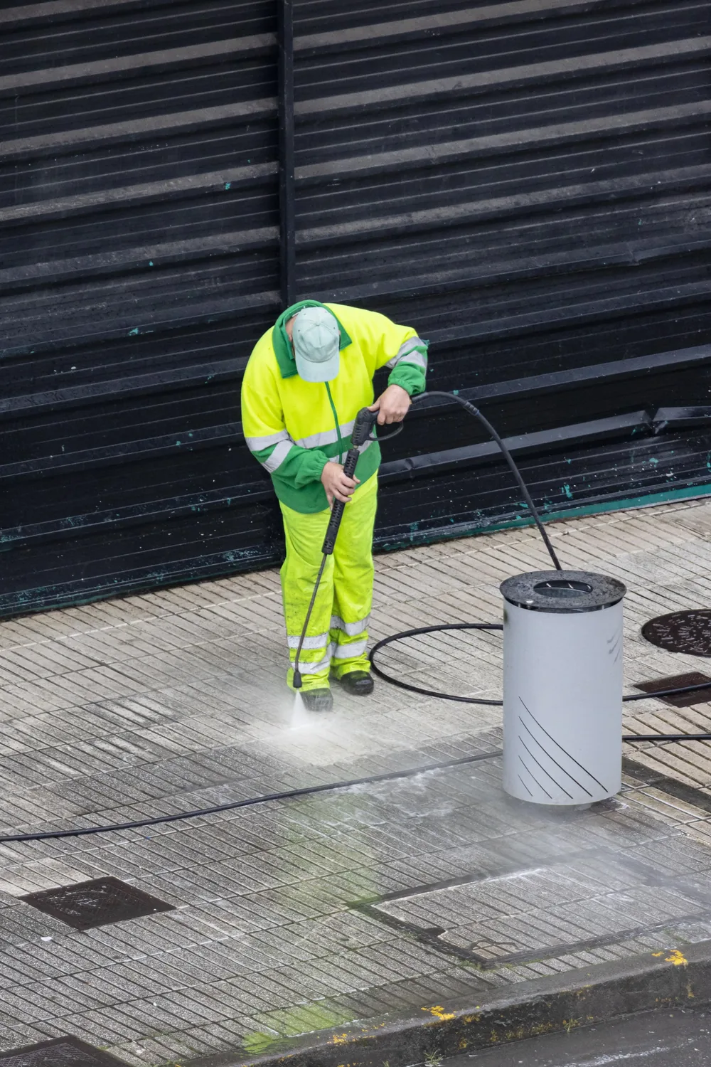 Crew member pressure washing a paved walkway